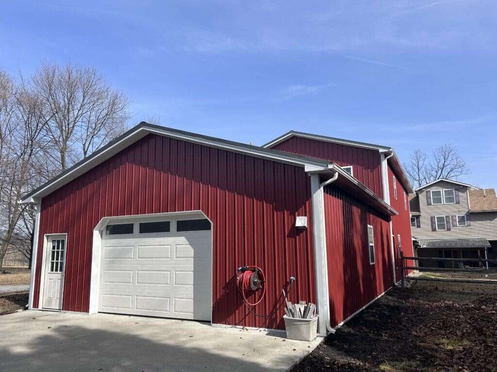 Red post-frame commercial building with white overhead door and attached two-story structure