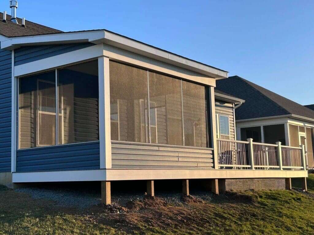 Completed screen room addition with full-length screened walls and composite deck on blue-sided home