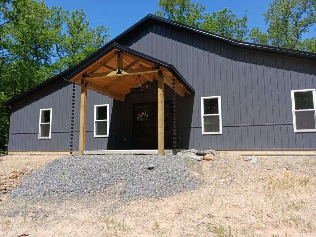 Custom barndominium-style home with dark grey vertical metal siding and timber entry porch