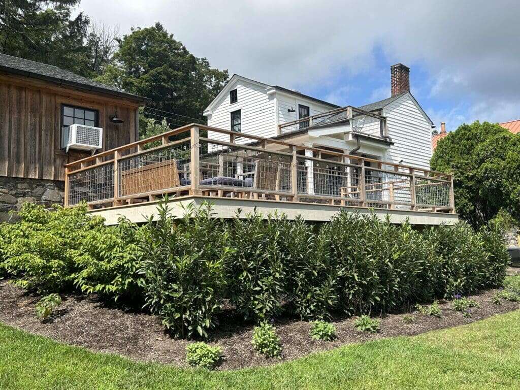 Elevated cedar deck with cable wire railing attached to white farmhouse