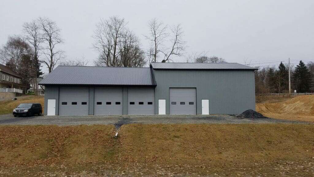 Grey-green post-frame commercial workshop with four overhead doors and walk-through entries