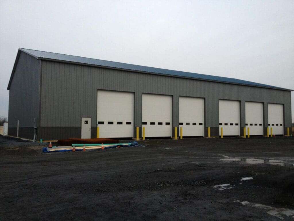 Completed grey metal commercial garage with four large overhead doors and yellow safety bollards