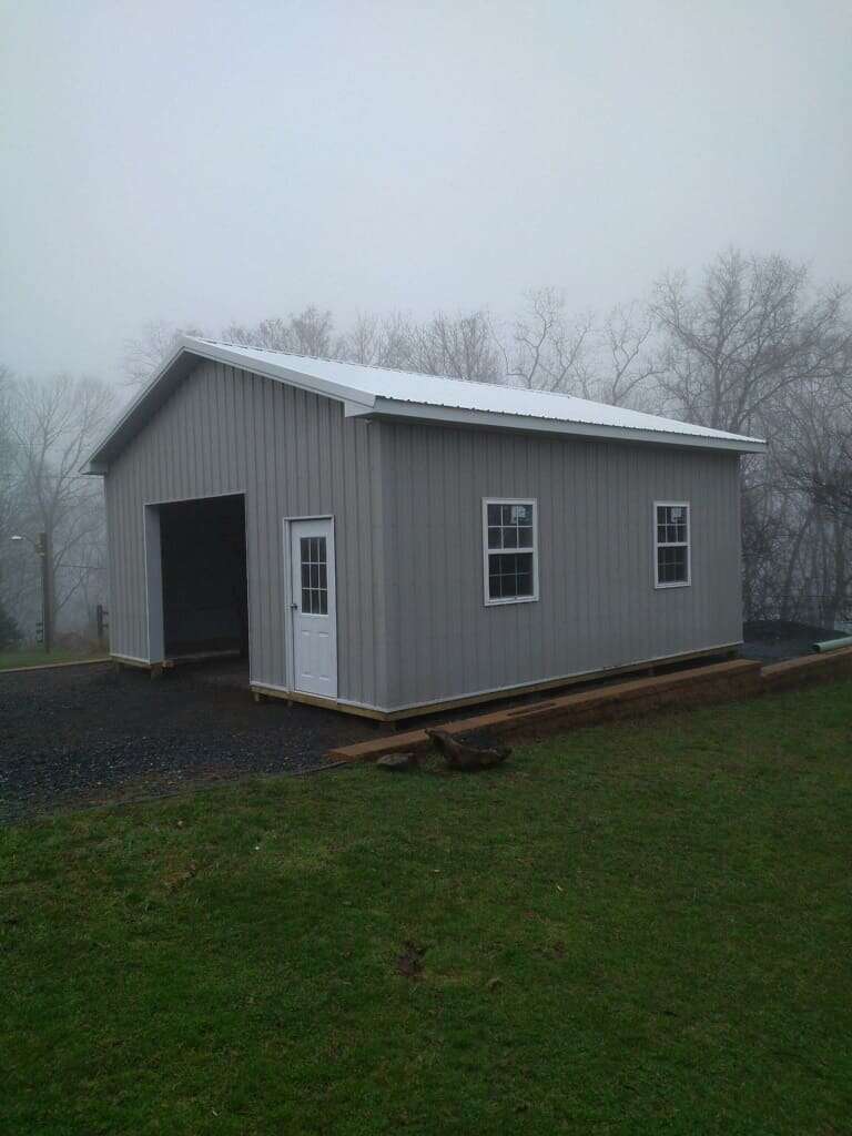 Single-bay post-frame garage with grey metal siding and white metal roof on a rural hillside property
