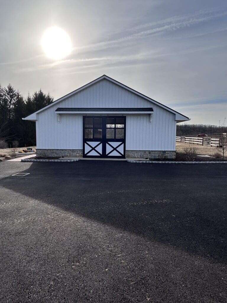 Front entry of white horse barn with black X-pattern sliding barn doors and stone wainscot base