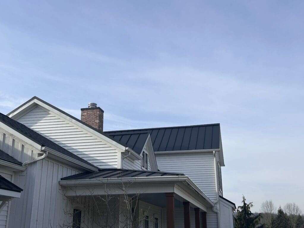 Dark standing seam metal roof on white residential home with brick chimney and covered porch