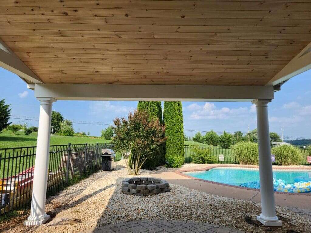 Covered patio with cedar tongue-and-groove ceiling, white columns, overlooking backyard pool and fire pit