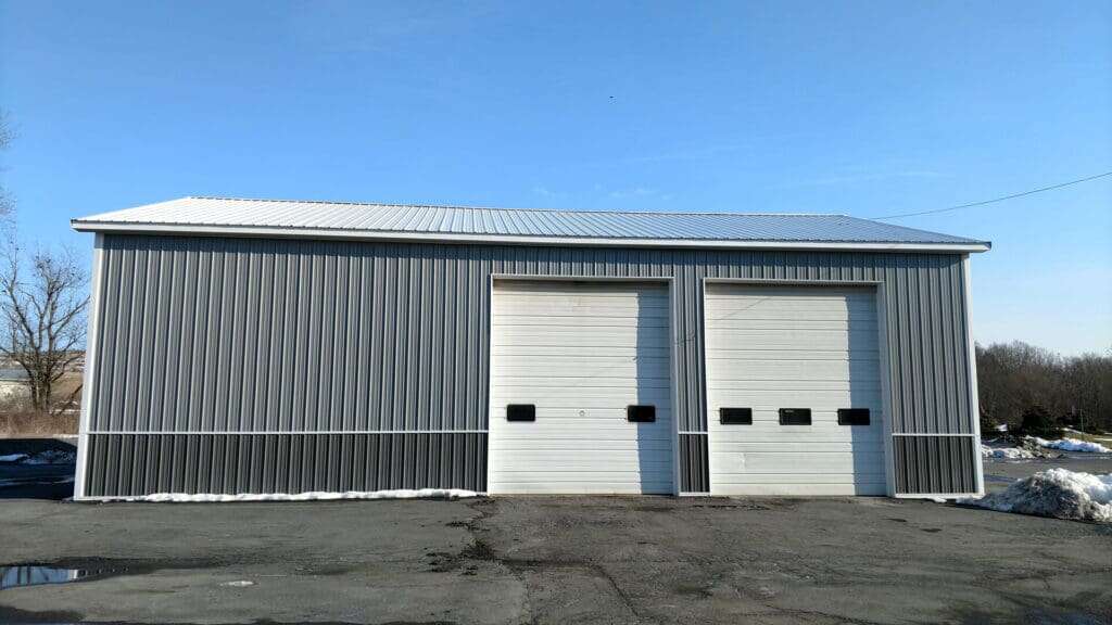 Completed grey metal commercial storage building with two overhead doors for landscape supply business