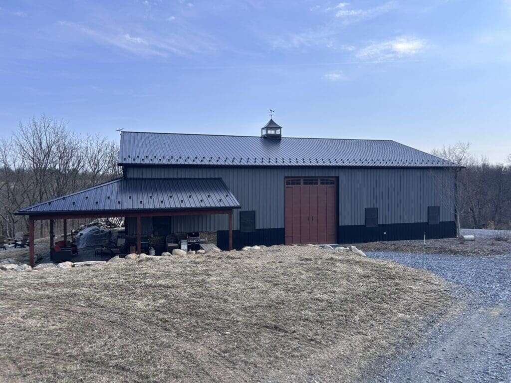 Large post-frame pole barn with grey metal siding, red barn door, lean-to, and ridge cupola