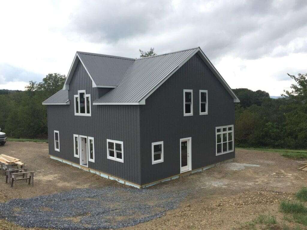 Two-story barndominium showing rear and side elevations with dark charcoal vertical metal siding, grey standing seam roof, and white-trimmed windows