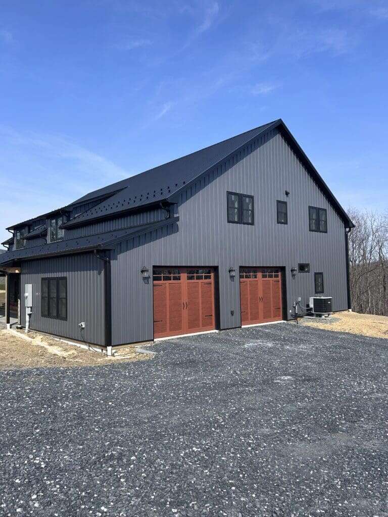 Garage elevation of custom barndominium with dark charcoal metal siding and carriage-style doors