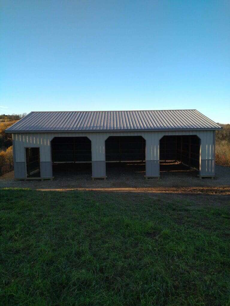 Open-front three-bay post-frame storage structure with grey metal siding and corrugated roof
