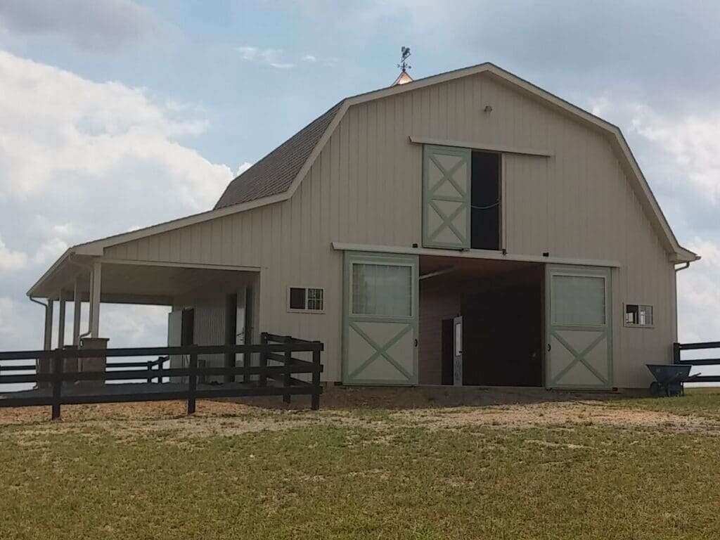 Gambrel-roof horse barn with sage green sliding doors, weathervane cupola, and attached lean-to