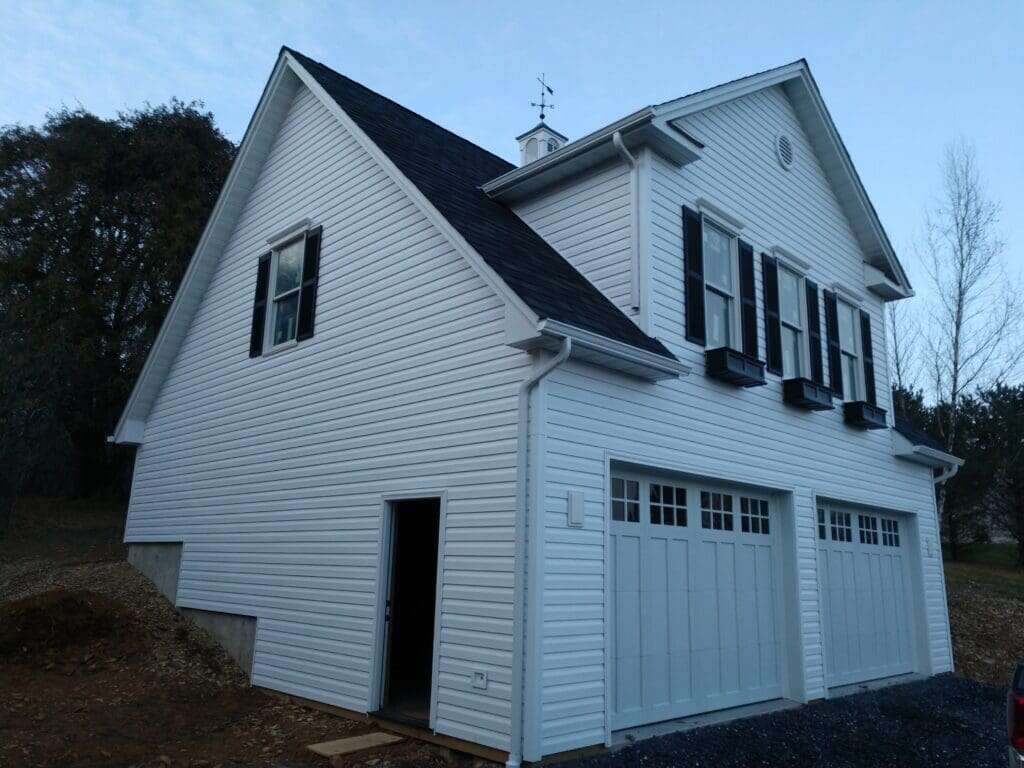 Two-story white vinyl garage with black shutters, carriage doors, and decorative cupola