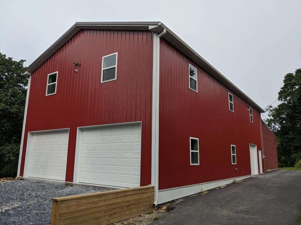 Large two-story post-frame garage with red metal siding, white overhead doors, and upper-level windows