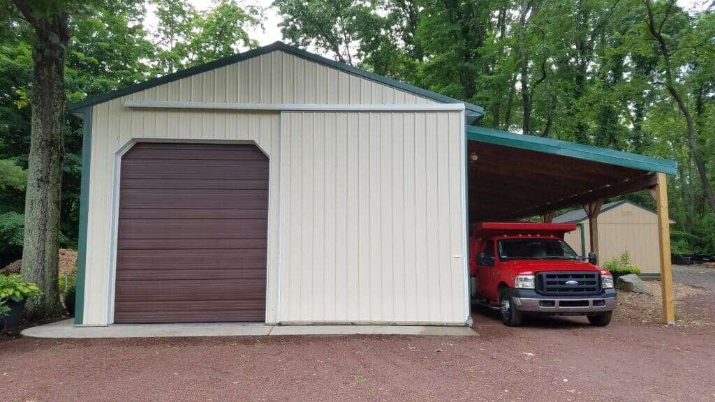 Post-frame garage with cream metal siding, brown roll-up door, green roof trim, and attached lean-to