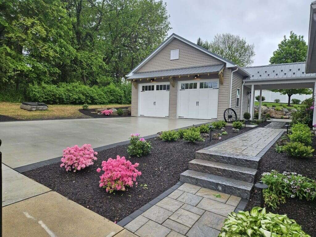 Two-car garage with tan siding, white carriage doors, cupola, breezeway, and landscaped driveway