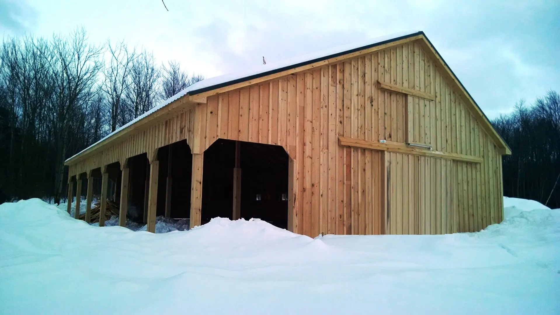 A barn with snow on the ground and trees in front of it.