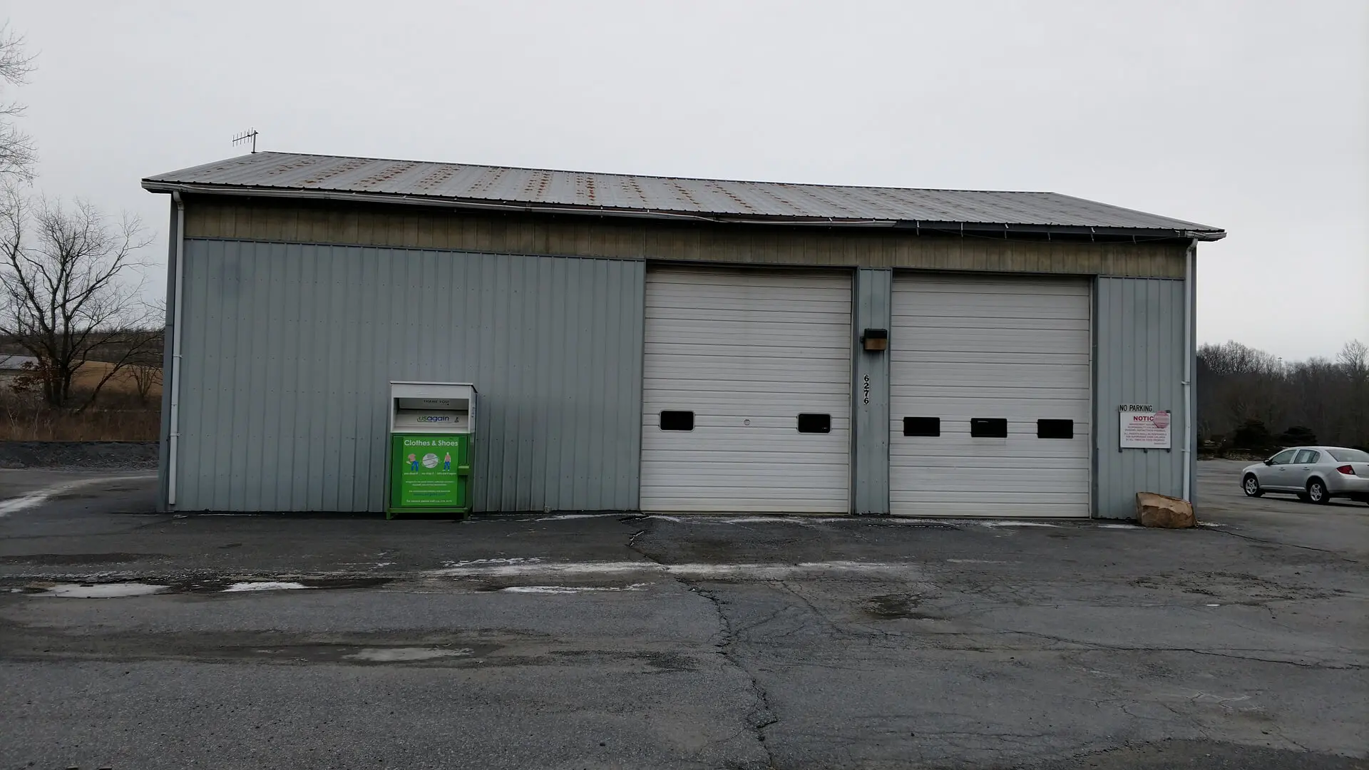 A green trash can sitting in front of two garage doors.