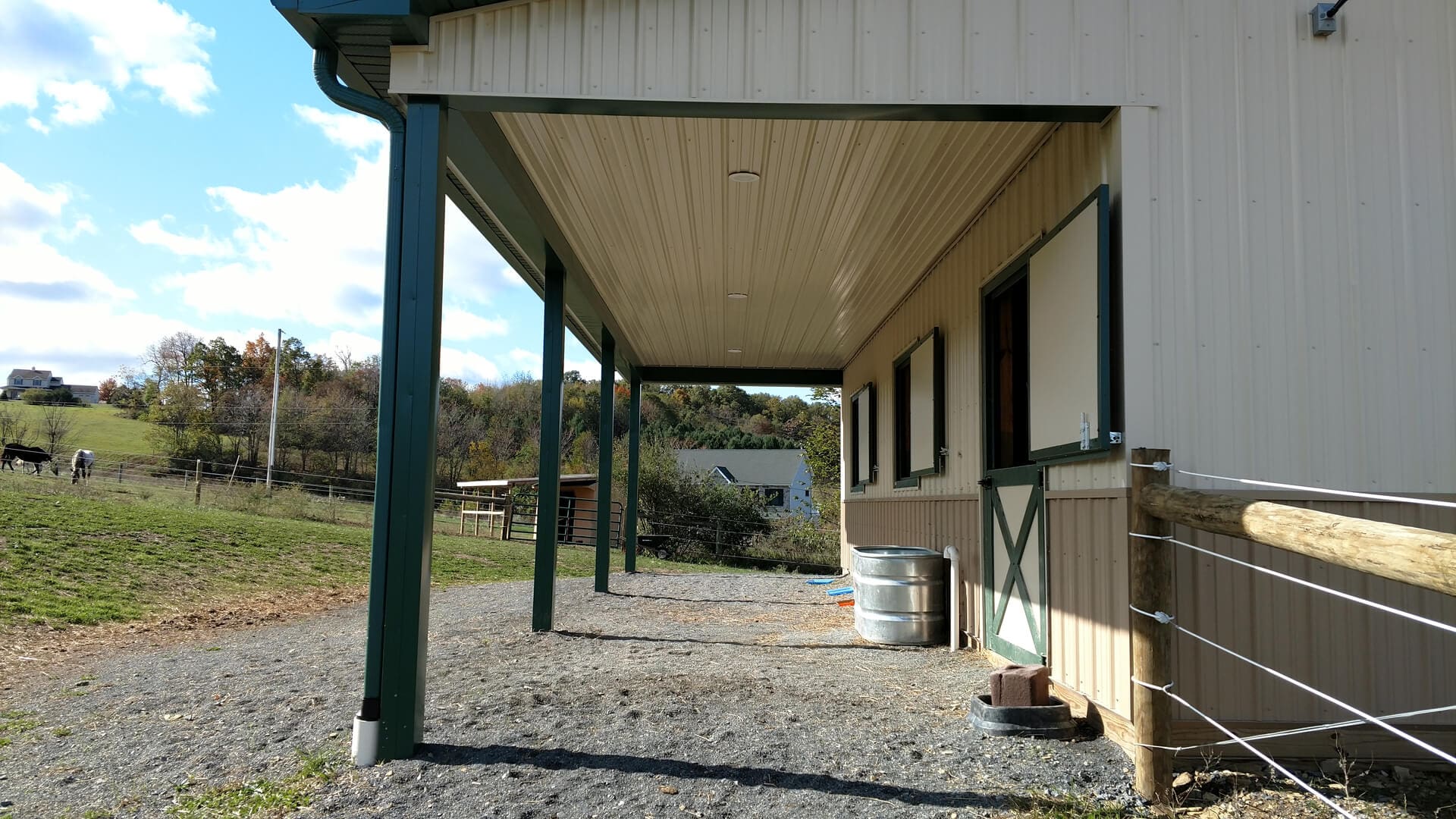 A barn with a covered area and two barrels.