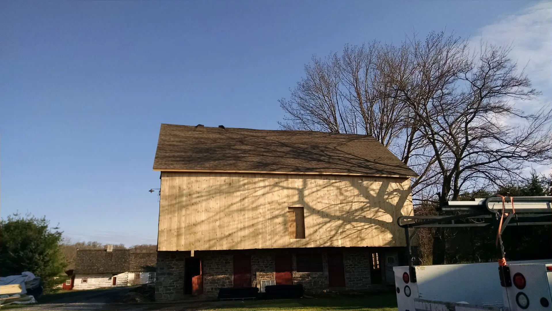 A large barn with a wooden roof and a tree in the background.