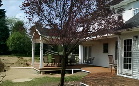 A tree is in front of the house and patio.